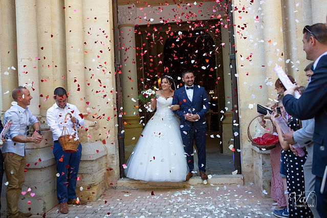 Sortie d'église sous une envolée de pétales rouges et blanc, thème du mariage