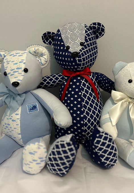 20-inch large memory bear handcrafted from navy and white patterned fabric with a red bow, shown beside smaller bears for size comparison. A fully customizable keepsake designed to showcase special clothing in a sentimental, lasting form.