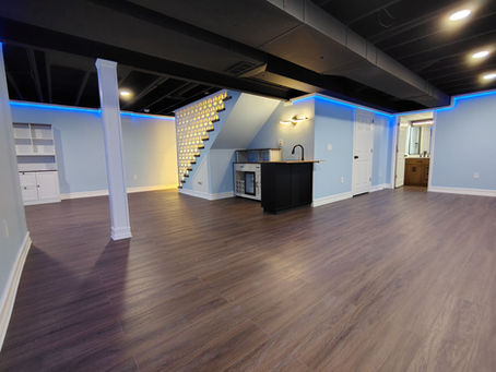 Wide-angle interior view of a modern luxury finished basement featuring commercial-grade LVP flooring and custom millwork wet bar built by SKY Living in Metro Detroit