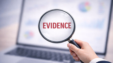 Magnifying glass highlighting the word evidence against a blurred laptop screen with business charts