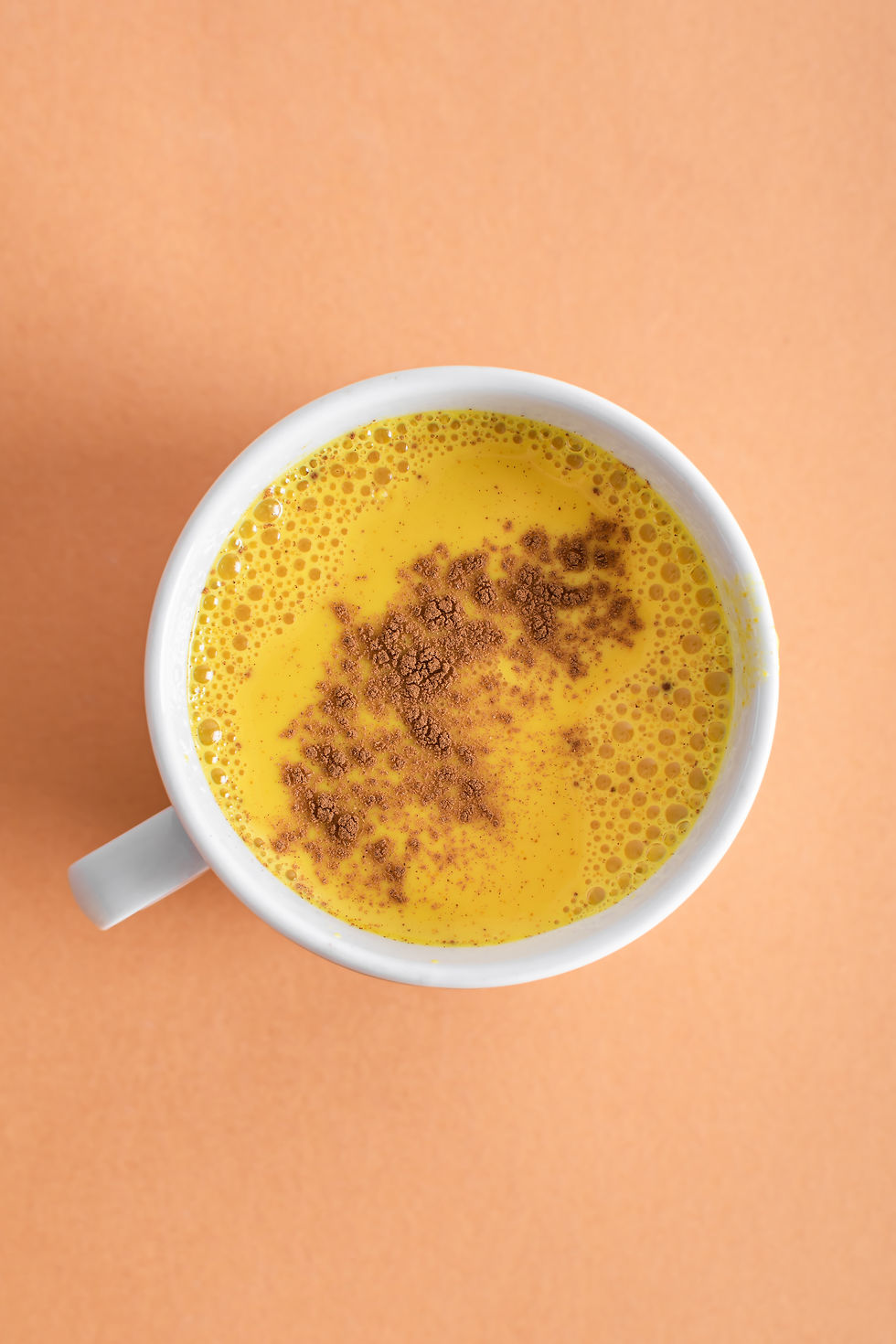 White mug of golden milk with turmeric and cinnamon powder on a light marinade background . Turmeric latte. Turmeric tea. Turmeric benefits for women. Antioxidants glutathione.