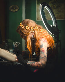 Tattoo session photography by Casey Gardner, UK photographer and videographer based in Somerset. This image captures Erin tattooing a detailed leg piece at Temperance Tattoo in Glastonbury. Documentary-style tattoo photography using the studio ring light to enhance shadow, texture, colour, black and grey ink detail, and the intense concentration of the tattoo artist at work. Creative studio and behind-the-scenes tattoo photography in Somerset, UK.