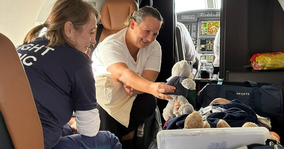 Adam's mum is showing him a teddy bear during his lia's wings air transfer. A Flight Nurse is looking on smiling.