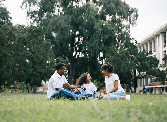 Two adults sitting in the grass with a young girl. They are all smiling.