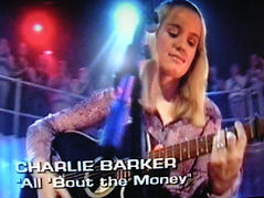 A screenshot of Charlie Barker's BBC 1 TV appearance, mid-performance in the TV studio. Charlie is wearing a purple top, playing a blue Takamine guitar and sat infront of a microphone.