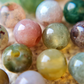 Close‑up of fancy jasper beads in soft greens, pinks, yellows, and purples, each with natural marbled patterns.