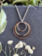 Copper, brass, and silver hoop necklace shown with dried flowers on a slate background.
