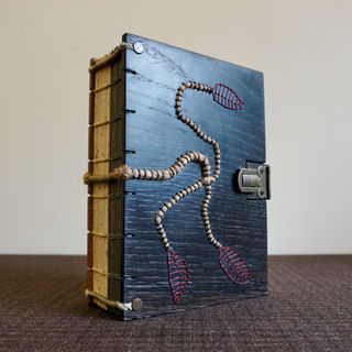 A handmade stained oak book with an exposed spine Greek binding and raised flax rope supports.