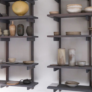 Wall-mounted shelves displaying finished ceramic pieces in natural tones inside the Enaes Maria studio