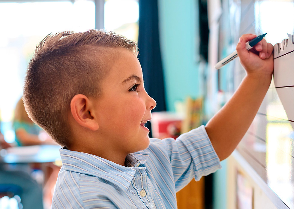 Young male student standing and drawing on a white board in a classroom