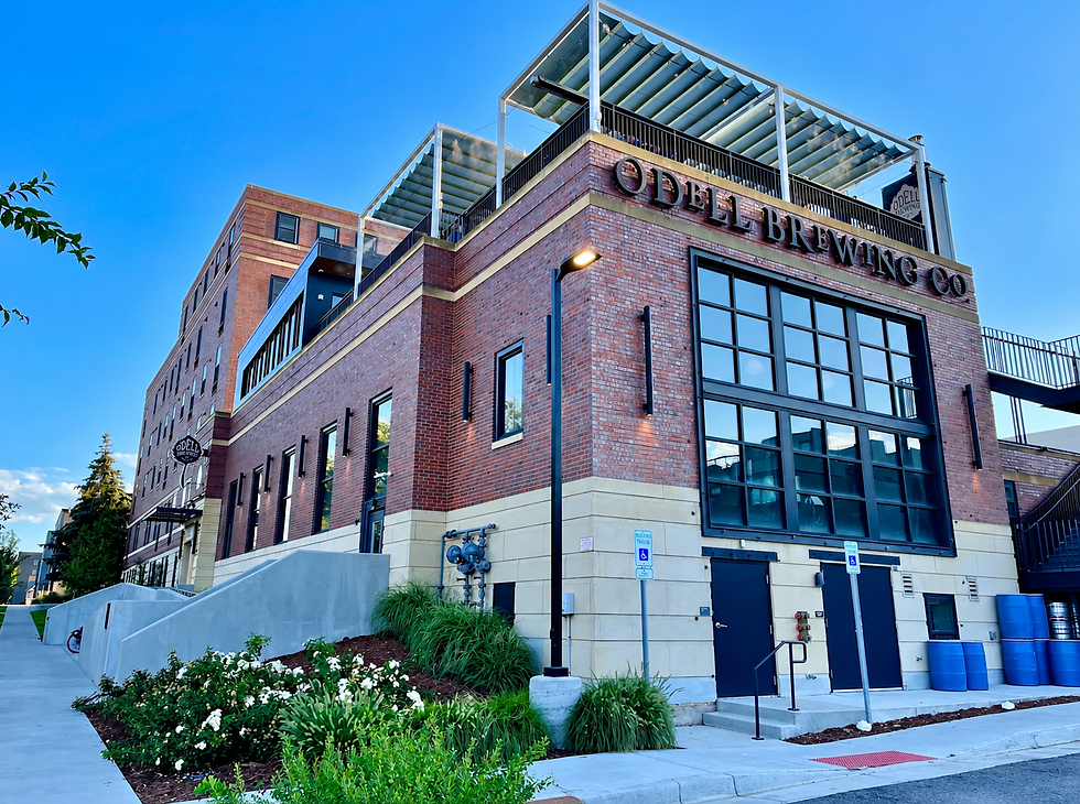 Brick ODELL Brewing Co. building with rooftop patio and glass windows under a bright blue sky, landscaped sidewalk in front.