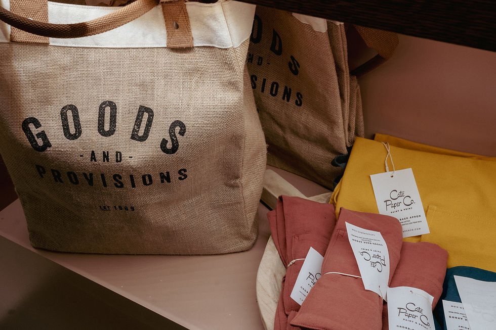 Retail display showing a 'Goods and Provisions' jute tote bag alongside colorful Café Paper Co. cloth napkins