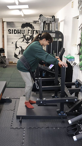 a female doing belts squats in a private gym with a personal trainer