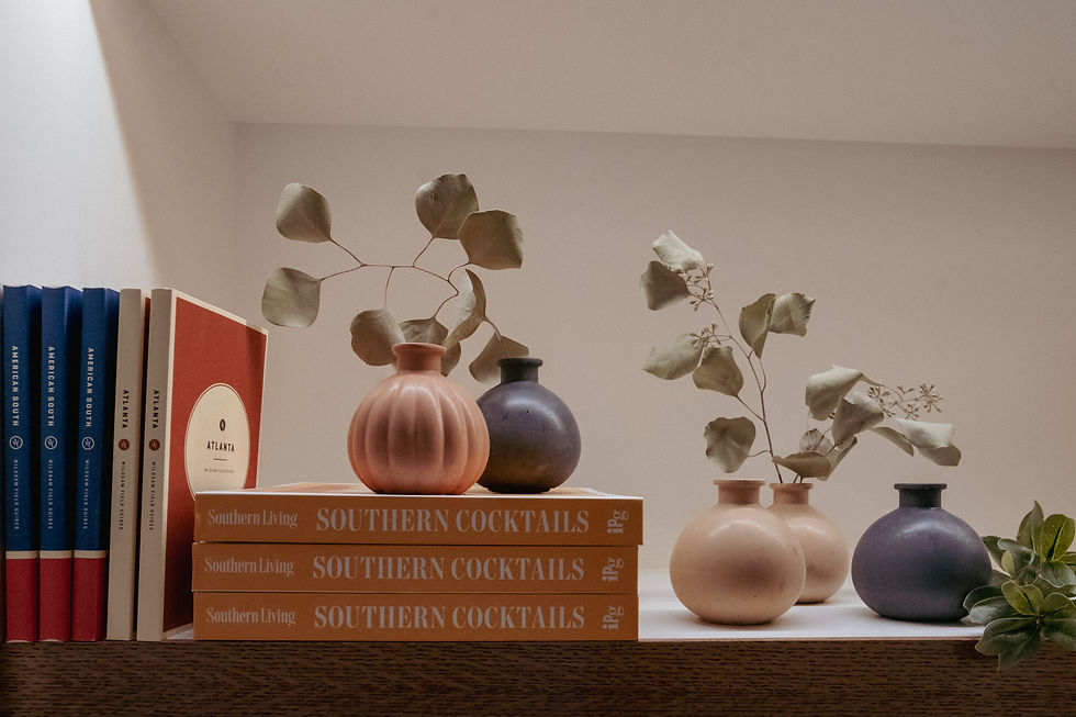 Bookshelf display with Southern Cocktails cookbooks, ceramic vases in pink, navy, and beige containing dried botanicals
