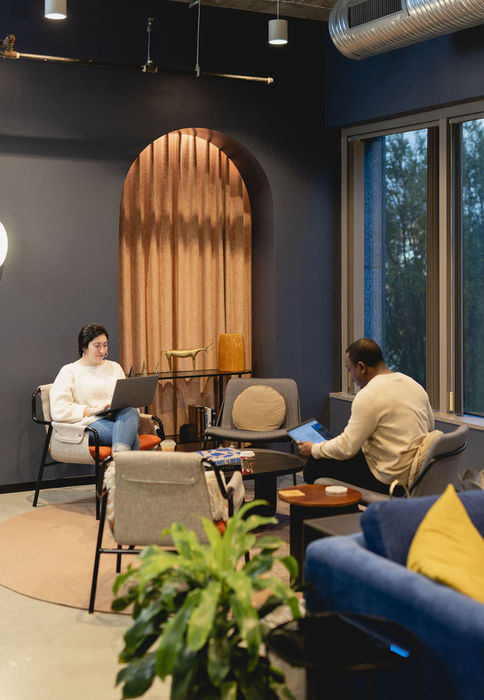 People working on laptops in a modern lounge with large windows and plants at The Commons 150 Fayetteville in downtown Raleigh.