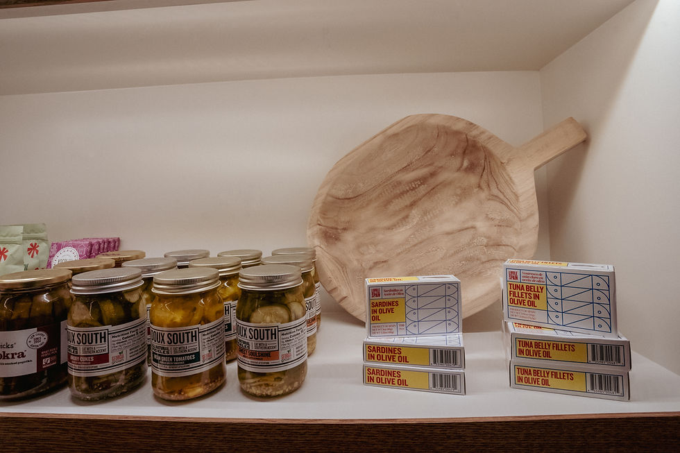 Retail shelf displaying Doux South pickled vegetables, tinned fish including sardines and tuna, and a decorative wooden serving board.