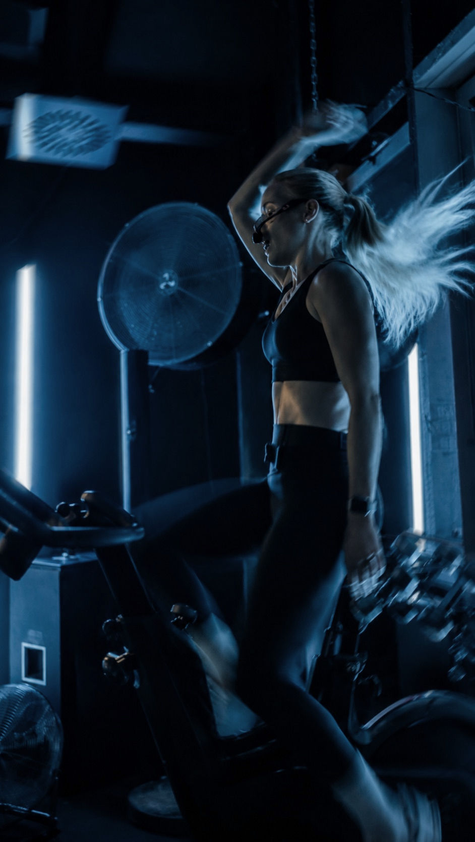 Woman riding hard on an indoor bike in blue studio light