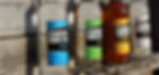 4 Bottles of Gotcha spirits lined up with a sun shining creating shadows on an old wooden barn.