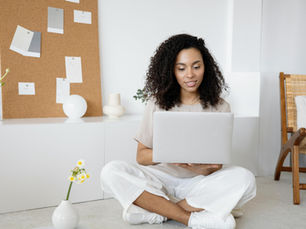 Girl on her computer in a white room, next to a yellow flower.