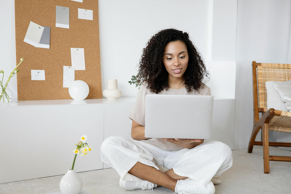 Girl on her computer in a white room, next to a yellow flower.