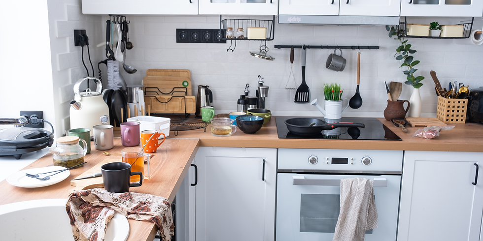 Cluttered modern kitchen with mugs, pots, utensils, kettle, and towels on wooden counters and a stovetop under white cabinets