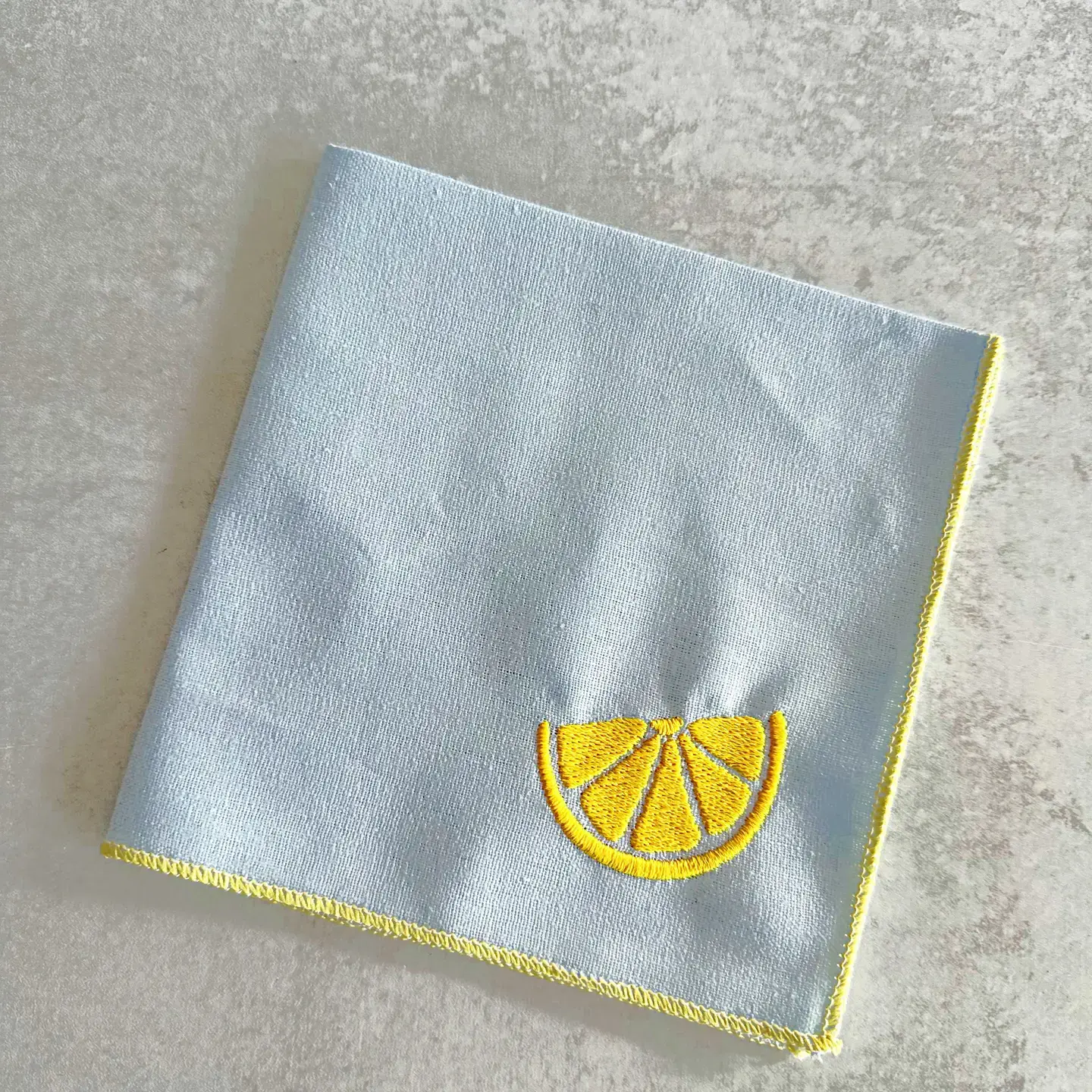 Blue cotton and linen blend cocktail napkin embroidered with a bright yellow lemon