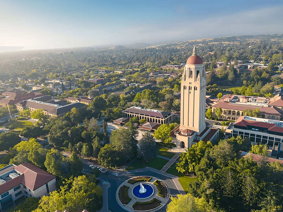 Aerial view of a tall beige tower with a red dome, surrounded by lush greenery and red-roofed buildings under a clear blue sky. Tranquil setting.