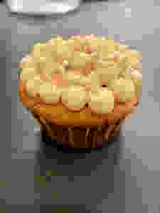 Finished cupcake decorated with a pale yellow buttercream and gold and pearl sprinkles