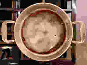 Foaming dark colored apple cider syrup in a small, shallow pot on the stove.
