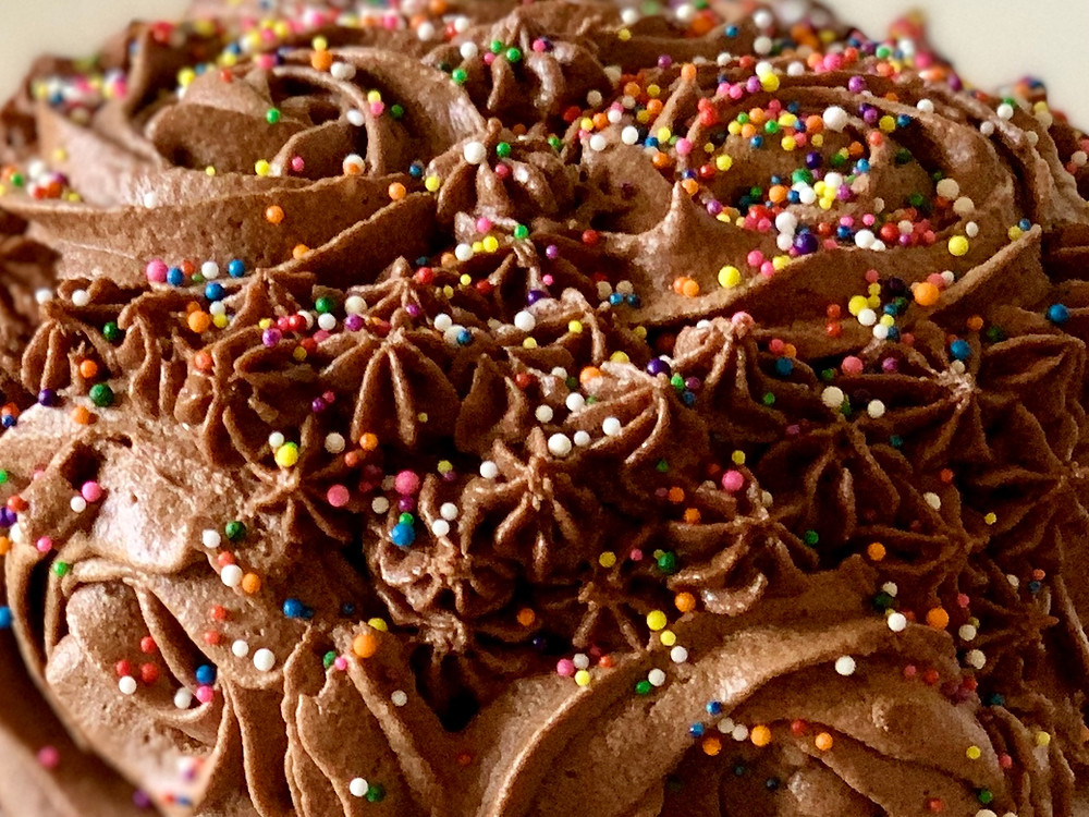 An extreme closeup of the frosting and sprinkles decorations on the cake. There is a slight color difference in various areas of frosting.