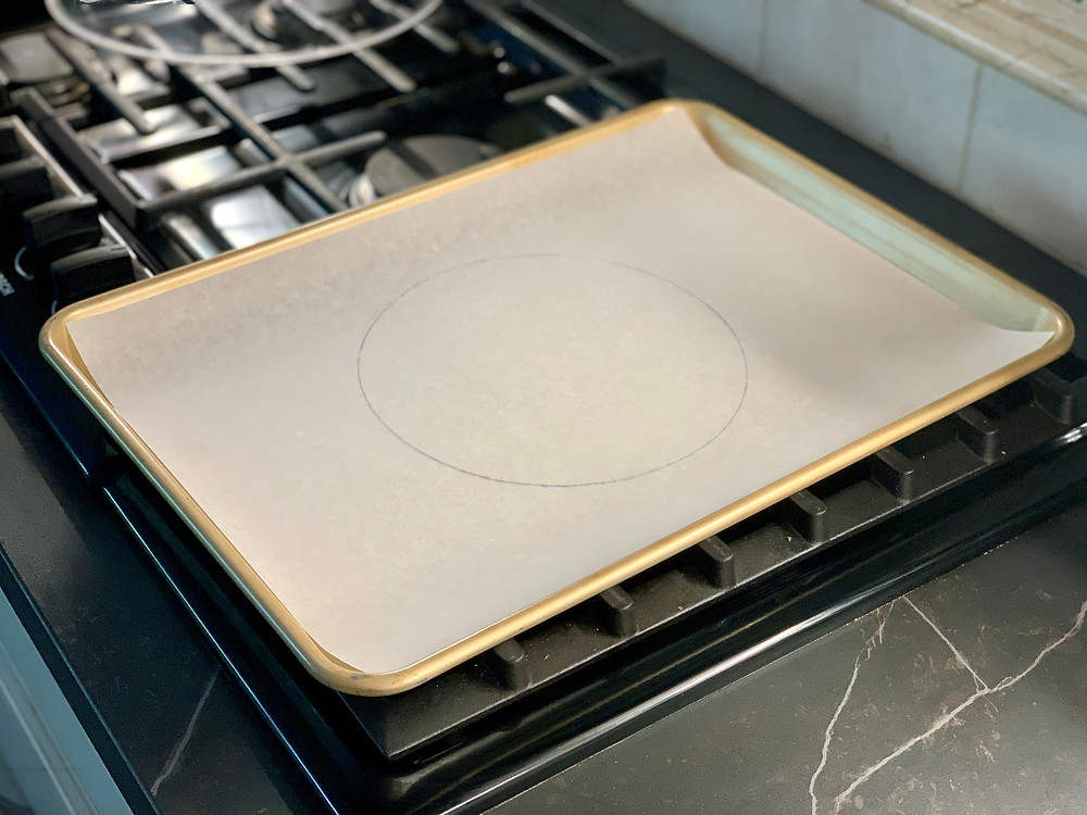 A circle drawn onto a piece of parchment paper in a gold colored baking sheet. It is sitting on an unlit stove.