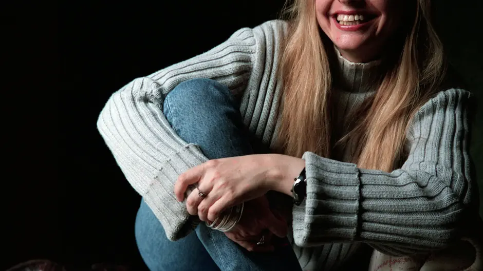 A photo of lawyer, writer, and forever New Yorker Elizabeth Wurtzel, a pretty, lively blonde woman in early middle age. She is wearing a beige sweater and jeans, and the photographer has captured her in a relaxed, smiling moment when her hands are clasped upon one knee. 