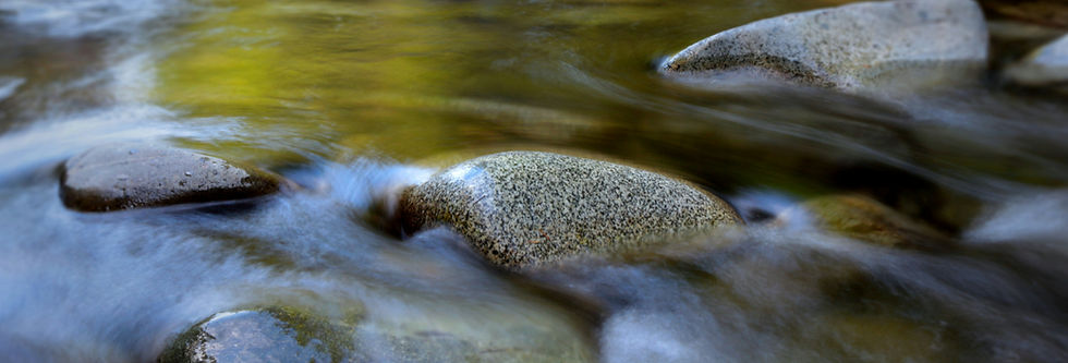Close-up of smooth rocks in a stream with water flowing over them. The water is blurred, creating a serene, tranquil scene.