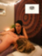 A person gives a massage to a woman on a purple blanket. Fairy lights and a mandala tapestry create a soft, relaxed ambiance. Photo credit: "MLD Photography."
