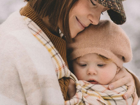 Mother wearing her baby in a sling, resting her head on baby's