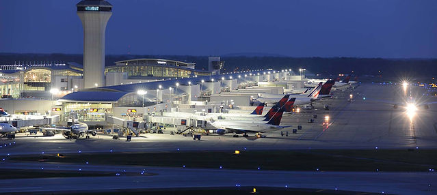 A snapshot of DTW airport at night. The outside of many Delta gates with planes next to them. The right of the images features two airplanes driving on the runway with their front lights bright.