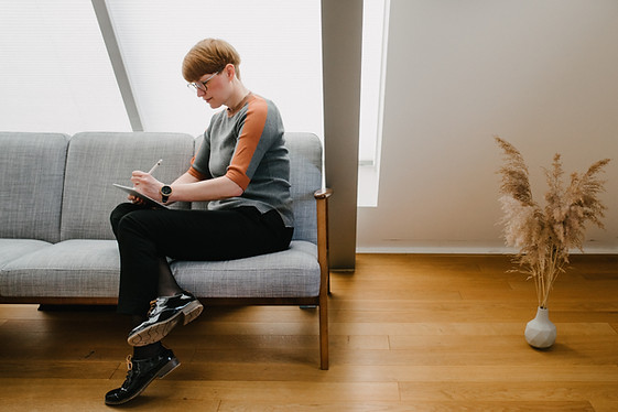Sara Dallmann, seitlich auf einem Sofa sitzend, macht sich Notizen