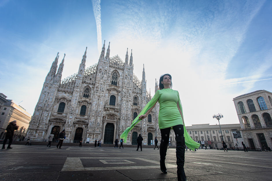 A woman in a bold green dress stands with quiet authority in the open piazza in front of Milan's Duomo cathedral — wide-angle personal branding photography that captures presence over pose