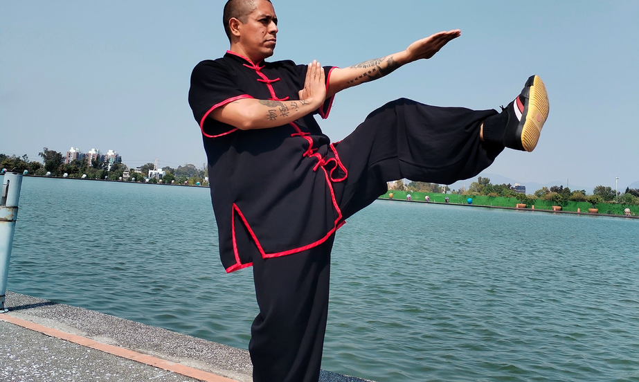 Practicante de Wushu realizando una patada de Wing Chun junto a un cuerpo de agua.