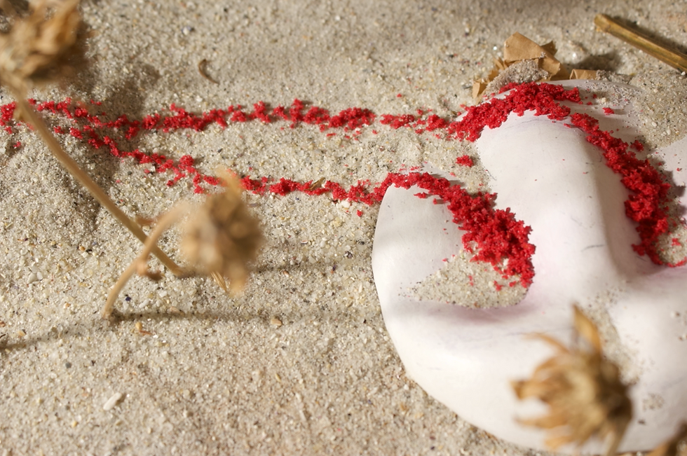 A large clay face mask lays in the sand. Its crying red thick sand, which crawls to a nearby rock.