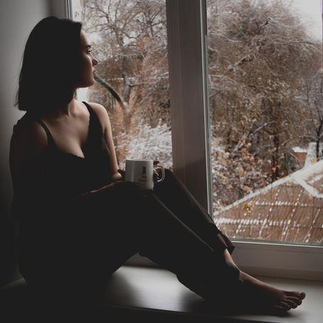 A cinematic, moody shot of a thoughtful woman staring pensively out of a window at dusk