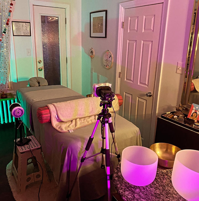 A photo of a camera and tripod set up in a living room with green and pink lights and singing bowls.