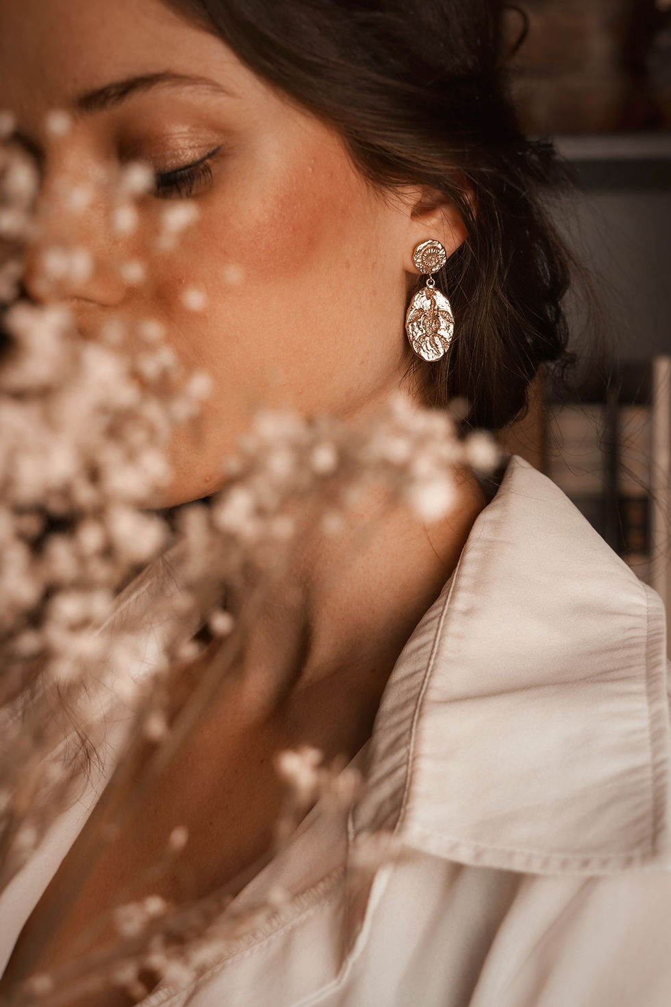Thumbnail: Beautiful woman wearing white shirt and gold dangly fossil earrings with blossoms