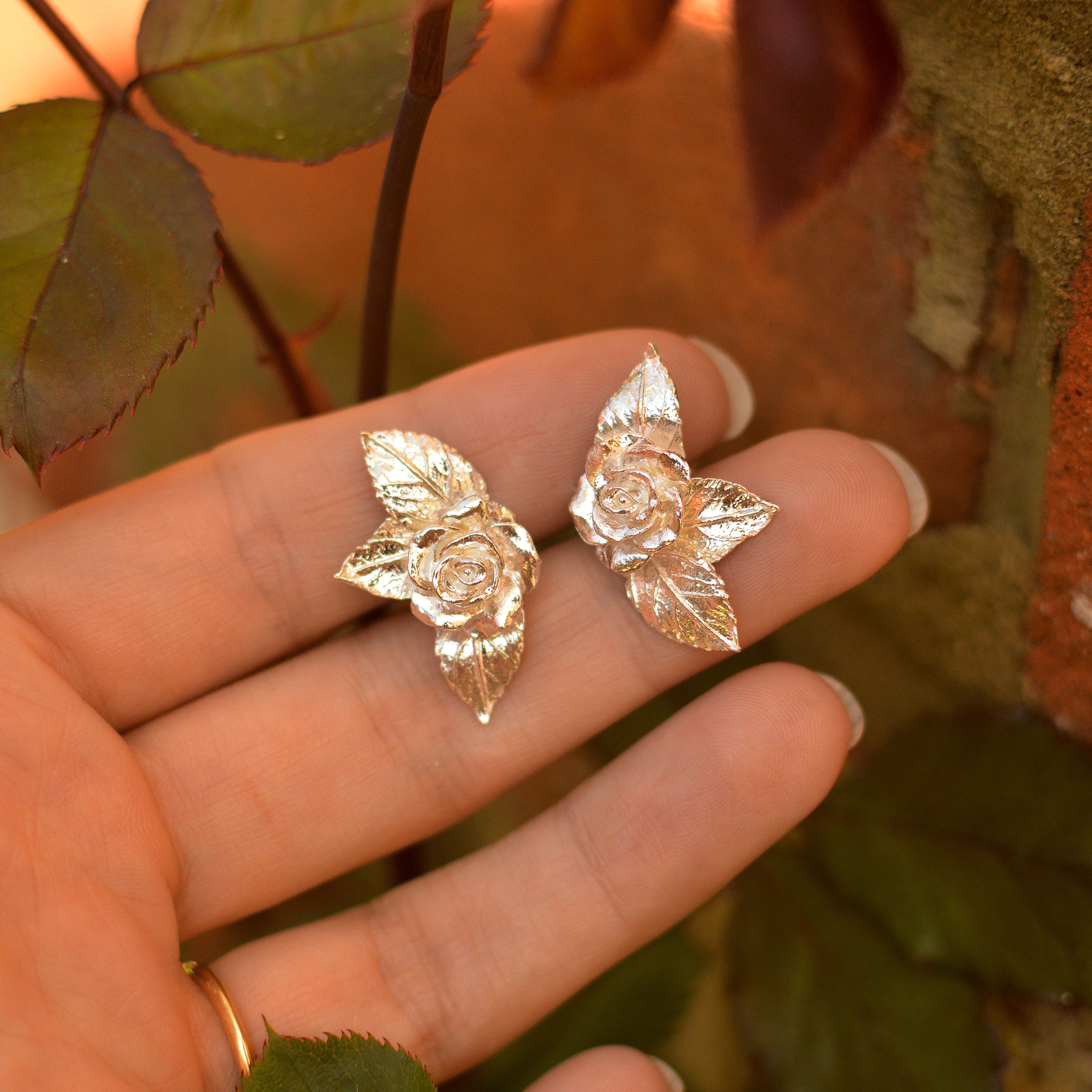Silver rose and leaf large stud earrings held in hand