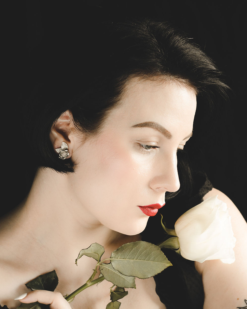 Thumbnail: Silver rose and leaf large stud earrings worn by black haired woman holding a rose