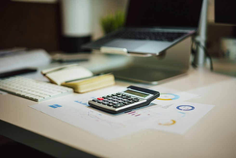Calculator resting on printed charts on a desk beside a laptop on a stand, a small notebook and a keyboard, representing a short-term rental host working out Vrbo payout math.