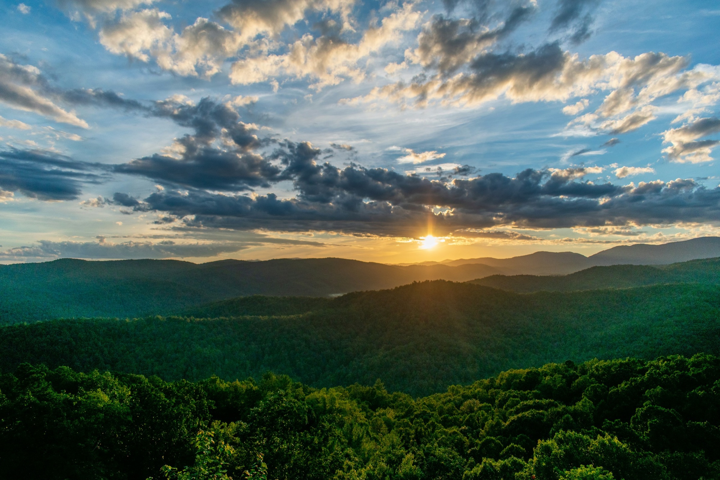 Sunrise breaking over forested Smoky Mountain ridges under scattered clouds