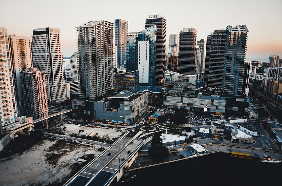 Dense cluster of Brickell high-rise condo and office towers in Miami at dusk, with a highway interchange and construction crane in the foreground