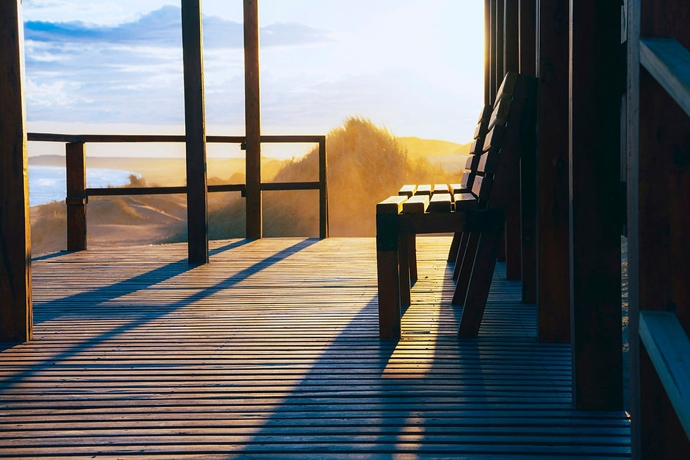Wooden deck in low golden light with a slatted bench, a railing, and grassy dunes beyond, representing a host weighing pricing tools.