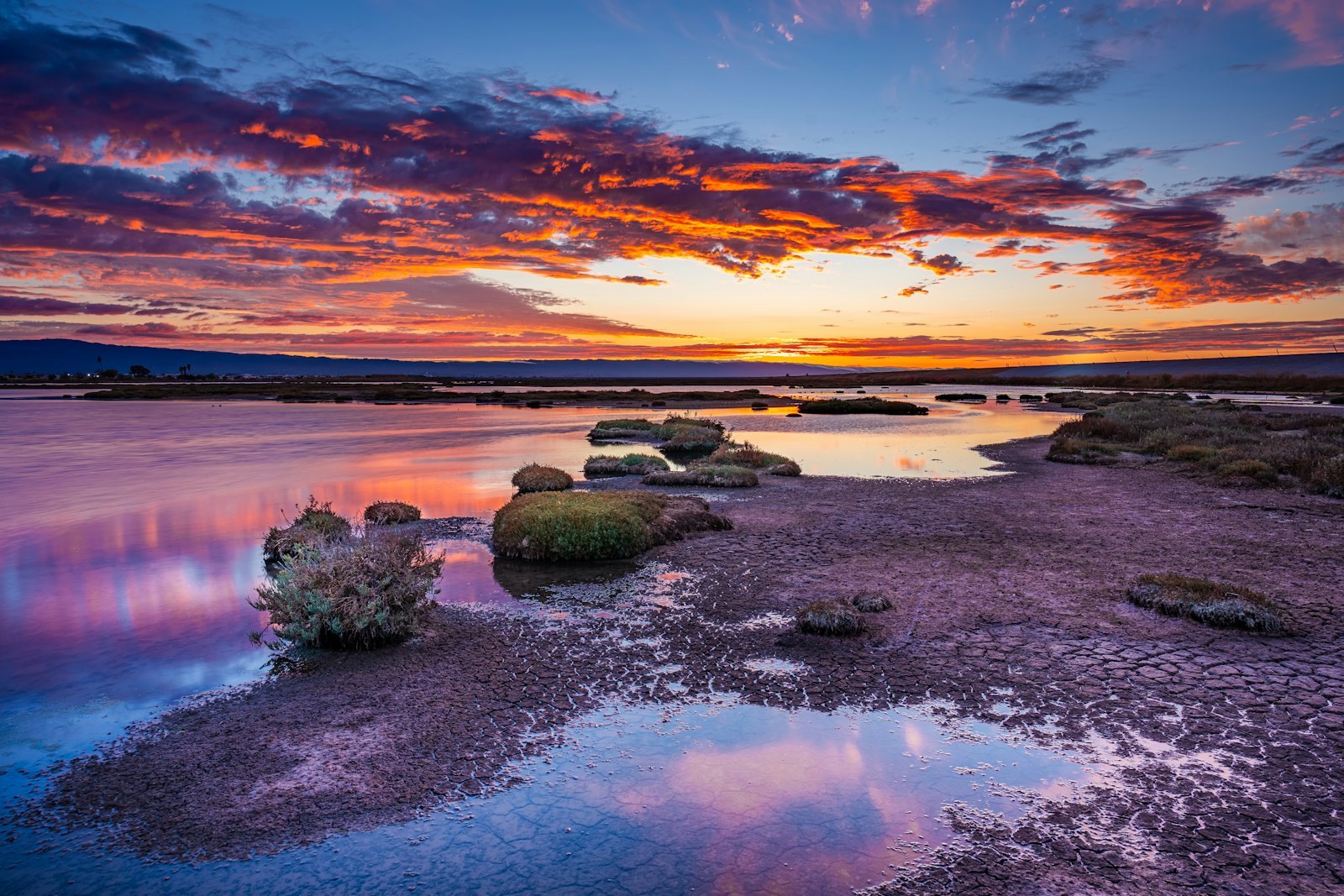 A sunset over a body of water with rocks in the foreground, empty of people